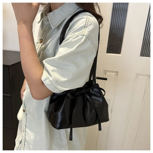 Detail of black leather underarm bag featuring drawstring bow design in a lifestyle setting