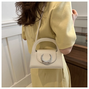 Detail of cream white small square handbag with silver moon-shaped buckle on a model