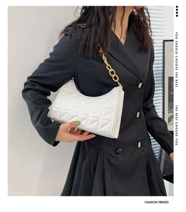 Close-up of white quilted leather bag with bold gold chain strap on a black blazer