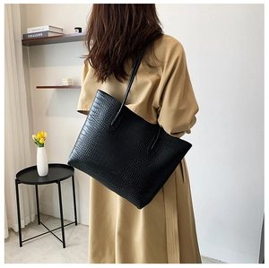Detail of black crocodile pattern tote bag shown with model in a minimalist setting
