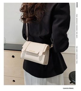 Detail of a cream-colored leather crossbody bag with a gold logo on a model