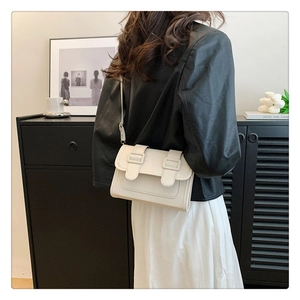 Side view of white minimalist square bag worn with black leather jacket and white dress