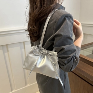 Chic silver underarm bucket bag with bow drawstring shown on a female model