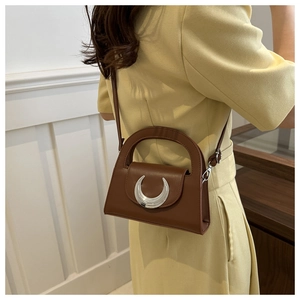 Detail of brown leather handbag with silver crescent buckle on yellow dress model