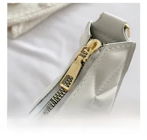 Close-up of golden zipper and quilted pattern on a white leather shoulder bag