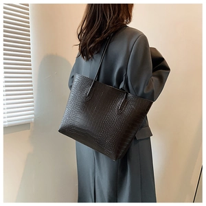 Close-up of a black crocodile-pattern tote bag worn over the shoulder by a model