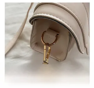 Close-up of polished gold hardware hook and neat stitching on beige leather handbag