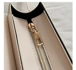 Detailed macro view of the gold metal zipper and premium leather texture on a beige handbag