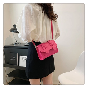 Rose pink faux leather crossbody bag with buckle flap shown on a model in a minimal setting