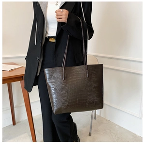 Detail of dark brown crocodile pattern texture and shoulder straps on a tote bag