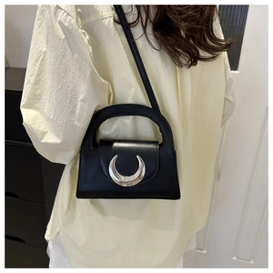 Close-up of minimalist black trapezoid handbag with polished silver crescent buckle detail
