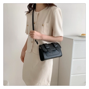 Detail of a black crossbody bag with double buckle closure on beige blazer suit