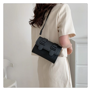 Detail of a vintage black leather crossbody bag with double buckle straps and flap cover