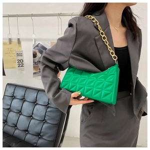 Detail showing emerald green quilted handbag with chunky gold chain strap worn by model