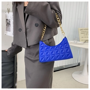 Detail of blue quilted shoulder bag with gold chain strap on a blazer-clad model