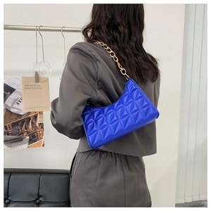 Close-up of bright blue quilted shoulder bag with gold chain strap on a blazer model
