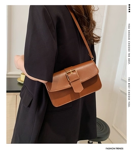Side view of a brown rectangular crossbody bag with a gold buckle worn by a model
