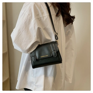 Detail shot of a black leather crossbody bag featuring gold letter printing on the front flap