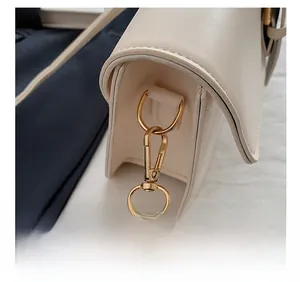 Gros plan sur l'anneau en D doré et le fermoir mousqueton du sac en cuir blanc crème