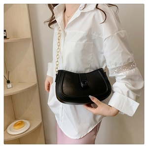 Detail of a black crescent shoulder bag with a gold chain strap on a model wearing white