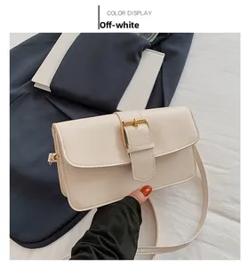 Detail of an off-white rectangular crossbody bag with a large golden buckle accessory