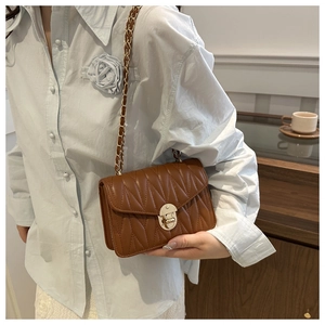 Close-up of quilted brown leather crossbody bag with gold chain strap on blue shirt