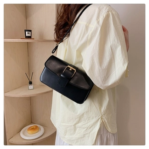 Détail d'un chic sac à bandoulière en cuir noir avec une boucle carrée dorée et un rabat lisse