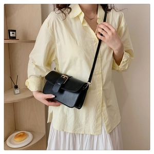 Gros plan du sac bandoulière en cuir noir avec boucle dorée porté sur une tenue chic