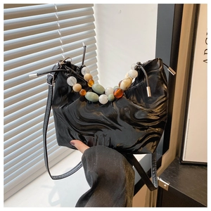 Detail of glossy black pleated tote bag with large colorful beaded handle and shoulder strap