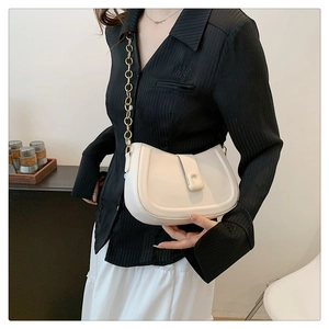 Chic off-white saddle bag with gold chain strap on shoulder of a model in studio