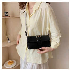 Sac baguette en cuir noir rétro avec boucle dorée porté par un mannequin en intérieur
