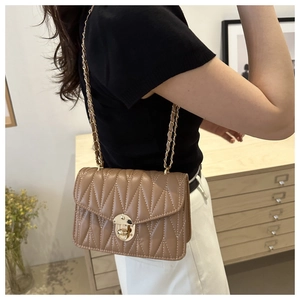 Side view of tan quilted crossbody bag with gold chain strap on domestic background