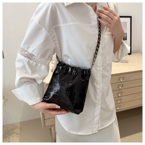 Close-up of black sequined crossbody bag with gold chain strap on lace shirt