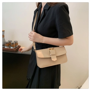 Détail du sac à rabat rectangulaire beige avec boucle dorée sur un tailleur noir