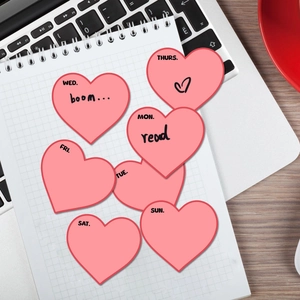 Pink heart-shaped weekly planner stickers with day abbreviations on white grid notebook