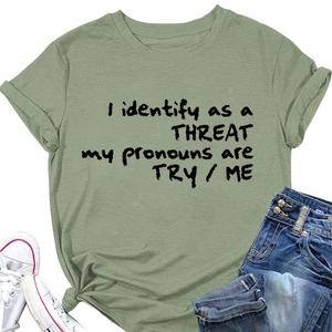 T-shirt vert sauge avec slogan 'I identify as a THREAT' à plat avec un jean bleu