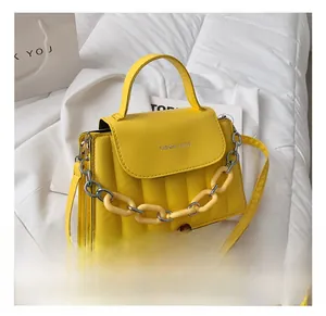 Detail of yellow quilted crossbody bag with a chunky chain and top handle on soft bedding