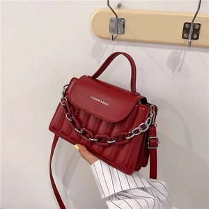Detail of red glossy leather handbag featuring vertical quilting and large chain link