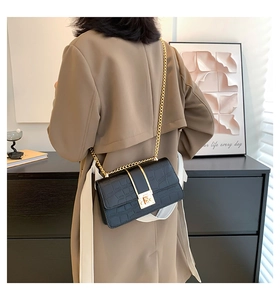 Modieuze zwarte crossbody tas met krokodillenprint en gouden ketting op een trenchcoat