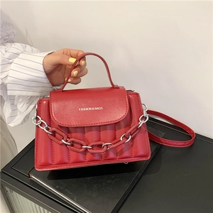 Close-up of red quilted handbag featuring matte chain detail and top handle strap