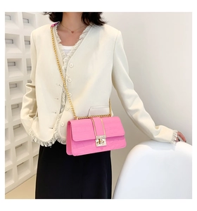 Close-up of bright pink crocodile pattern crossbody bag with gold chain and lock detail