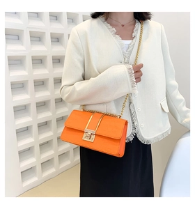 Orange croc-embossed crossbody bag with gold chain strap shown on model's shoulder