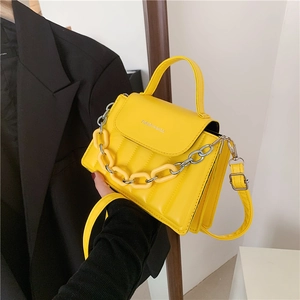 Detail of yellow quilted crossbody bag with decorative chain shown held by model