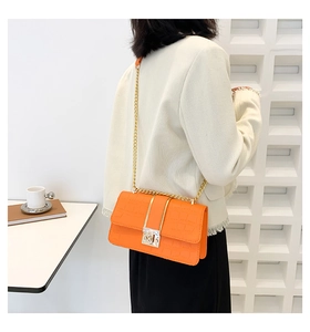 Detail of orange embossed crocodile pattern mini bag with golden chain and clasp