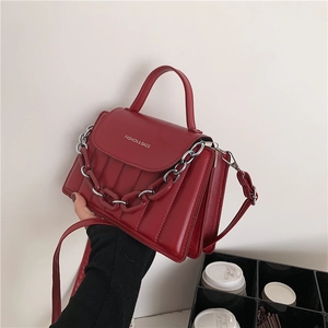 Detail of red crossbody bag featuring fashion text, metal chains, and accordion side structure