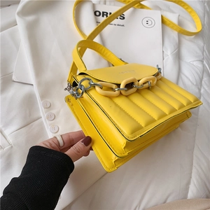 Detail of yellow quilted crossbody bag with chunky chain on a white blazer