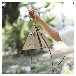 Détail d'un sac triangulaire beige avec fermeture à cordon et clous de protection au fond