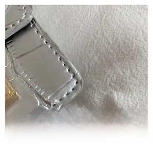 Gros plan du sac argenté avec motif crocodile embossé et détails de couture soignés