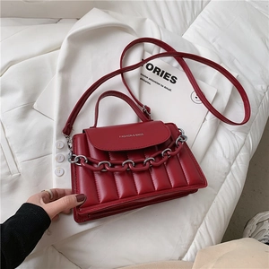Close-up of red quilted leather handbag with gold chain detail and textured pleats