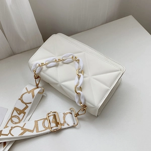Detail of white quilted crossbody bag featuring textured fabric strap and gold chain